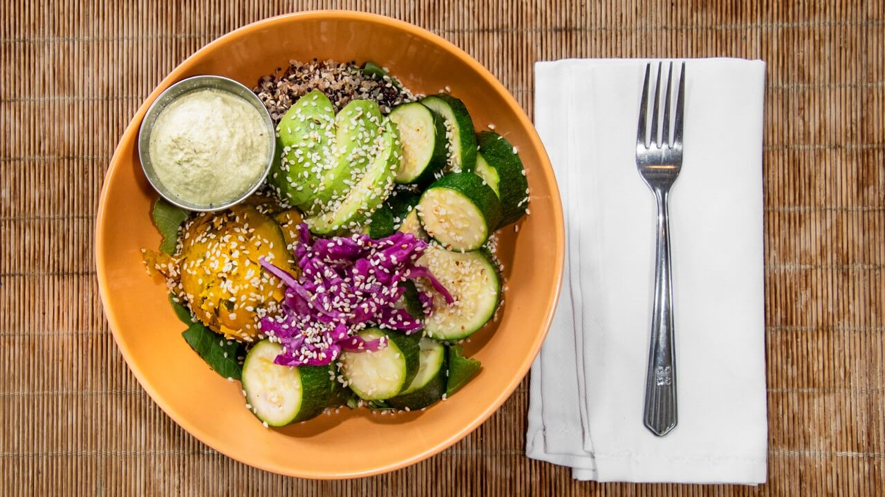 Lucky Squash Party bowl with squash, cabbage, and a side of dressing on a wooden table with a fork and napkin.